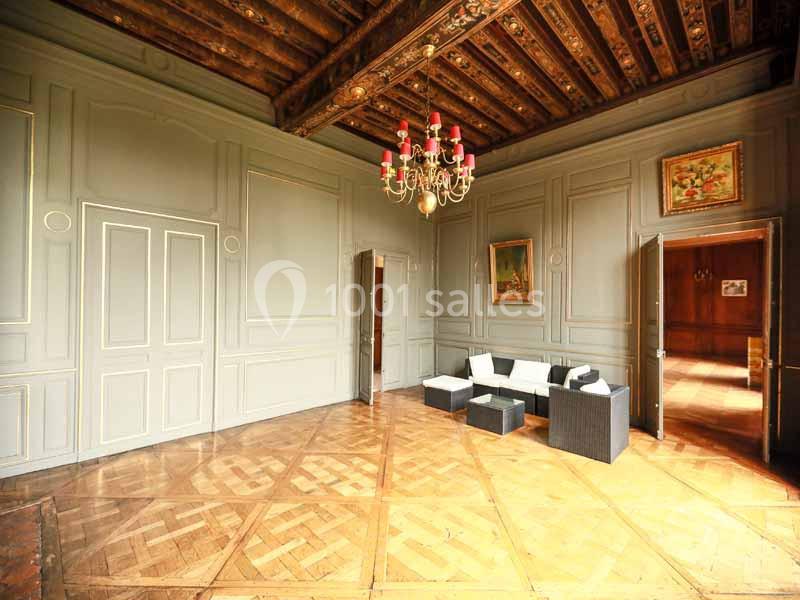 Salle lumineuse avec parquet en bois, murs ornés de moulures, plafond décoré et mobilier moderne près d'un lustre.
