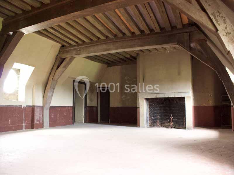 Grande pièce vide avec poutres en bois apparentes, cheminée en pierre et murs partiellement peints en rouge.