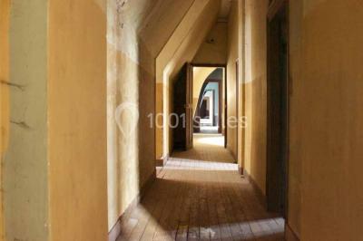 Bâtiment ancien avec façade décrépite, entouré d'une cour herbeuse et d'arbres dénudés en arrière-plan.