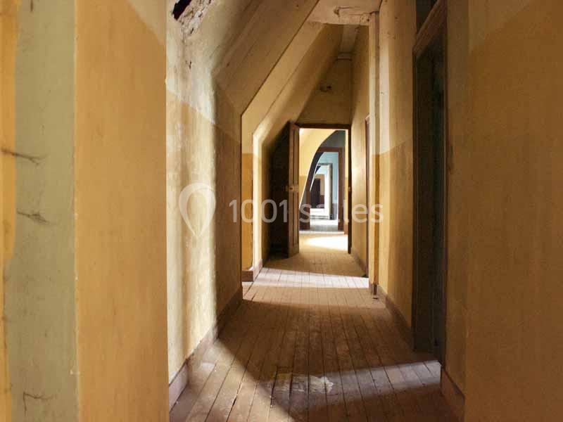Couloir ancien avec murs jaunis, sol en bois usé et portes ouvertes laissant entrevoir d'autres pièces.