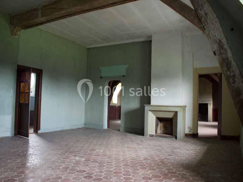 Une pièce vide avec un sol en carreaux, une cheminée, des murs clairs et des poutres apparentes au plafond.
