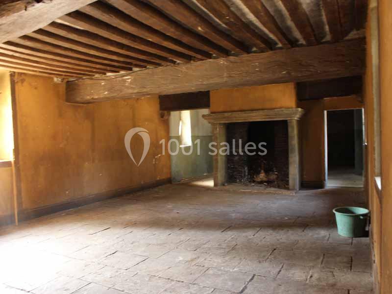 Pièce vide avec murs et plafond en bois, cheminée en pierre, sol en dalles, et un seau vert dans un coin.