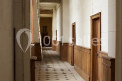 Bâtiment ancien avec façade décrépite, entouré d'une cour herbeuse et d'arbres dénudés en arrière-plan.