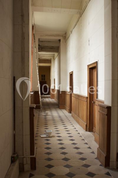 Couloir étroit avec sol en carreaux noirs et blancs, murs clairs, boiseries et portes en bois, éclairé naturellement.