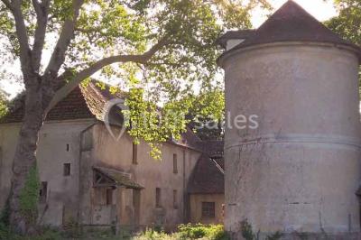 Bâtiment ancien avec façade décrépite, entouré d'une cour herbeuse et d'arbres dénudés en arrière-plan.