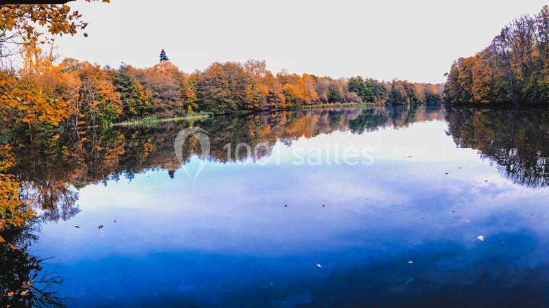 Reflet des arbres aux couleurs automnales sur la surface calme d'un lac entouré de végétation.