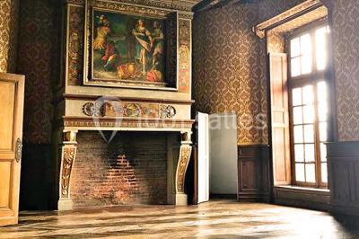 Bâtiment ancien avec façade décrépite, entouré d'une cour herbeuse et d'arbres dénudés en arrière-plan.
