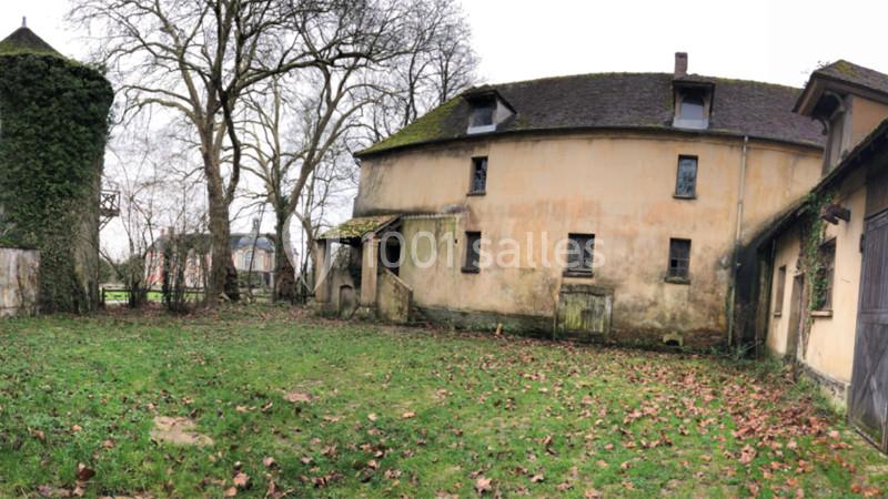 Bâtiment ancien avec façade décrépite, entouré d'une cour herbeuse et d'arbres dénudés en arrière-plan.