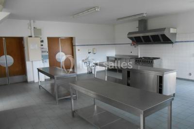 Cuisine professionnelle avec plans de travail en inox, hotte d'extraction, évier et carrelage mural blanc.