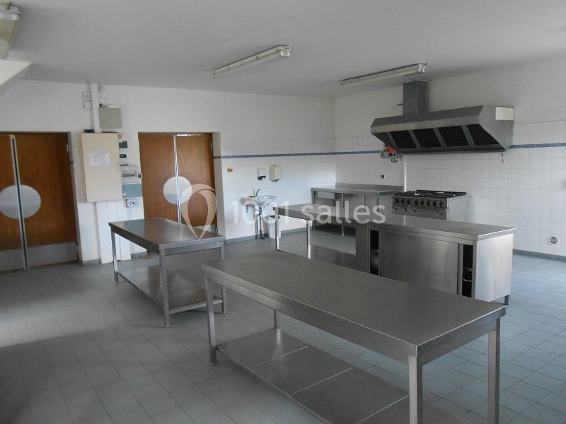 Cuisine professionnelle avec plans de travail en inox, hotte d'extraction, évier et carrelage mural blanc.