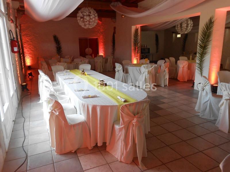 Salle de réception décorée avec des tables drapées de blanc, chemins de table jaunes et éclairage chaleureux.