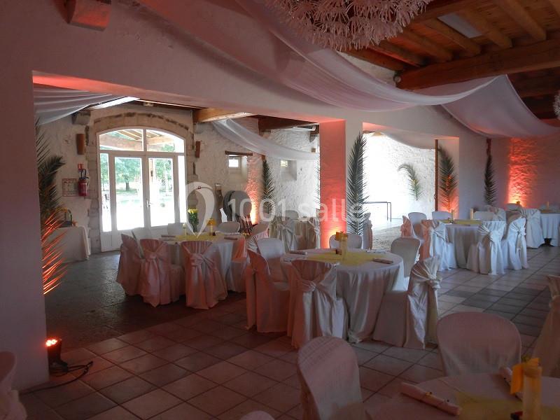 Salle de réception décorée avec des tables rondes, nappes blanches, chaises houssées et éclairage chaleureux.