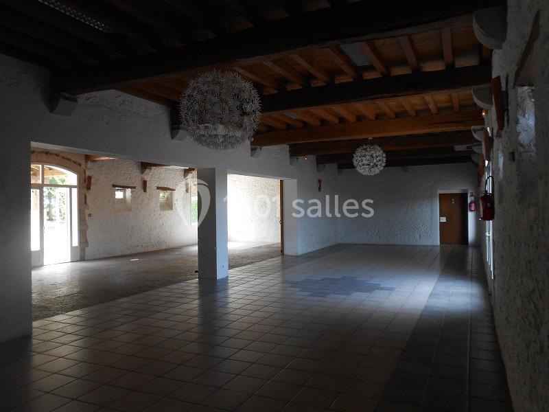 Salle vide avec sol carrelé, murs blancs, poutres en bois au plafond et luminaires suspendus.