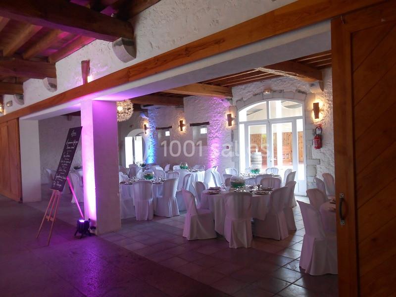 Salle de réception décorée avec des tables rondes dressées, chaises blanches et éclairage coloré.