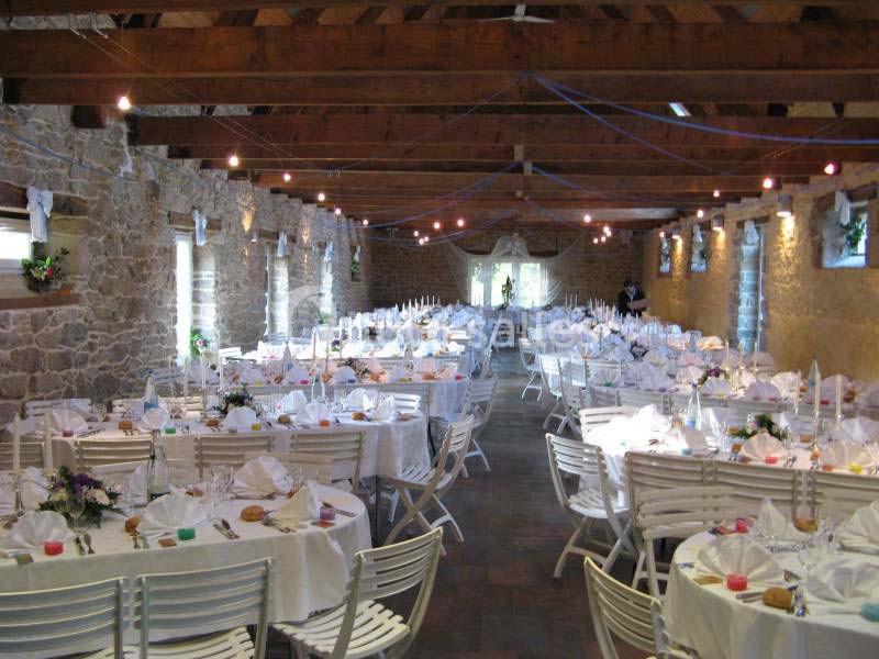 Salle en pierre avec des tables rondes dressées pour un événement, décorée de nappes blanches et éclairée par des guirlandes.