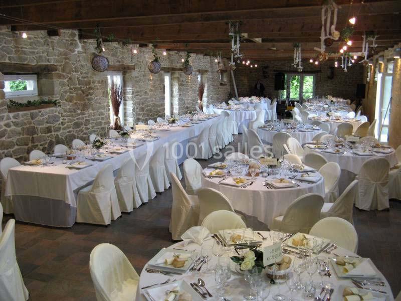 Salle de réception en pierre avec tables rondes et rectangulaires dressées pour un événement.
