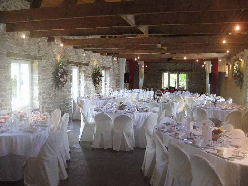 Salle de réception en pierre avec tables rondes dressées, nappes blanches et décorations florales.