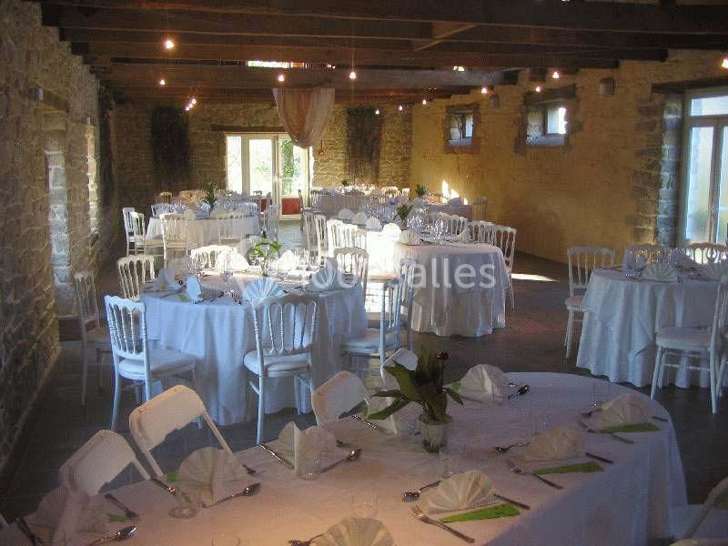 Salle de réception en pierre avec tables rondes dressées de nappes blanches, chaises assorties et décoration élégante.