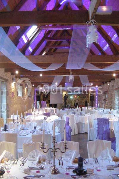 Salle de réception décorée avec des nappes blanches, des voilages suspendus et un éclairage violet.