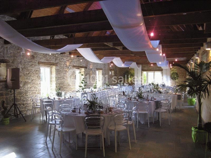 Salle de réception en pierre avec tables dressées, chaises transparentes et décoration suspendue en tissu blanc.