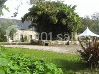 Maison en pierre avec toit en ardoise, entourée de végétation, une tente blanche visible à droite.