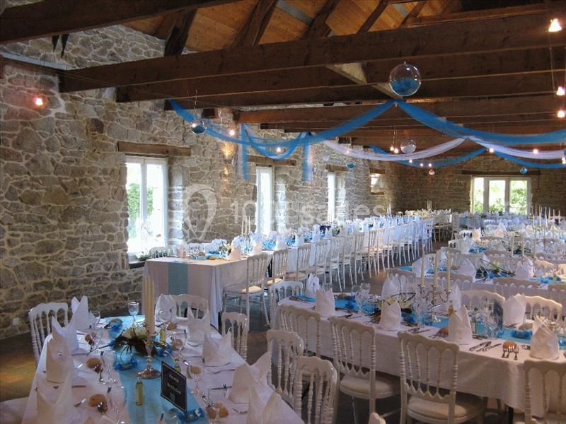 Salle de réception en pierre avec tables décorées en blanc et bleu, préparées pour un événement festif.