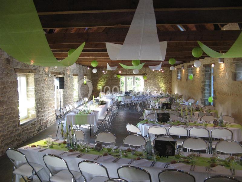 Salle décorée pour un événement, avec tables dressées, chaises blanches et guirlandes vertes suspendues au plafond.