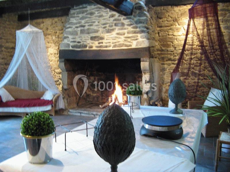 Cheminée en pierre allumée dans une pièce rustique avec table décorée et fauteuil sous un voile.