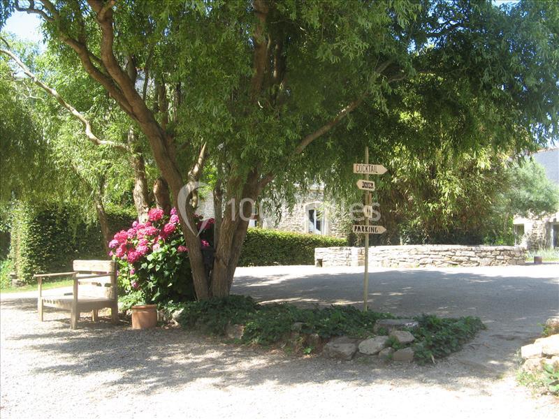 Allée ombragée avec banc en bois, hortensias en fleurs et panneaux directionnels près d'un arbre.