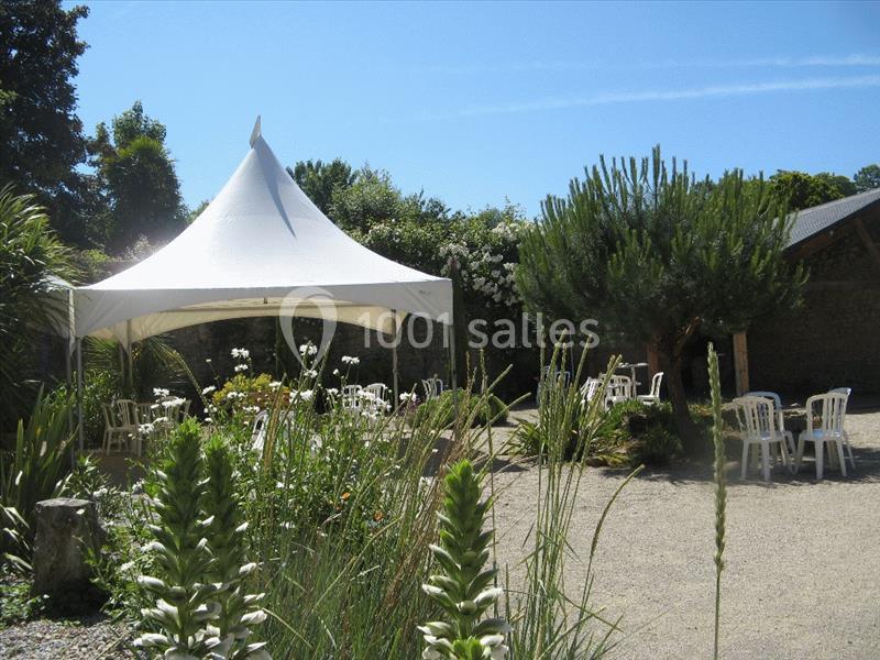 Tente blanche installée dans un jardin avec des chaises blanches disposées sur un sol gravillonné.