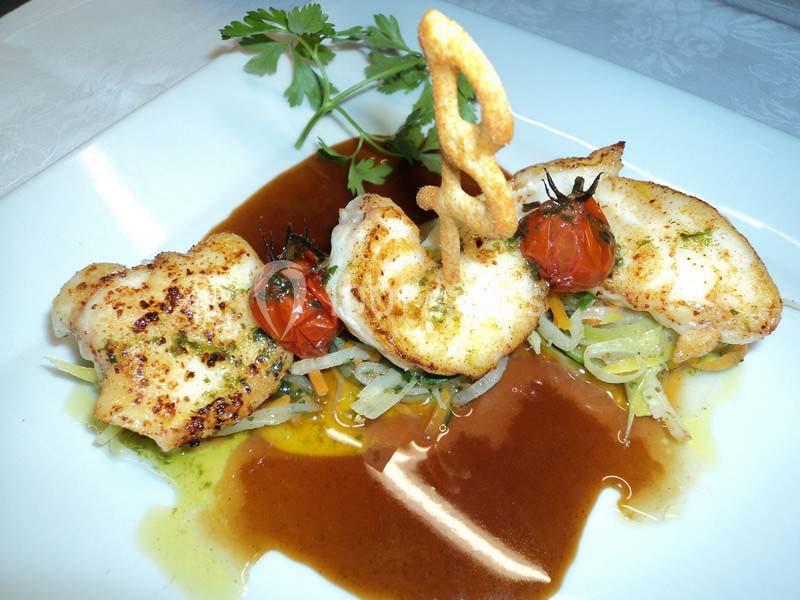 Filets de poisson grillés avec tomates cerises, légumes croquants et sauce brune, garnis d'une herbe fraîche.