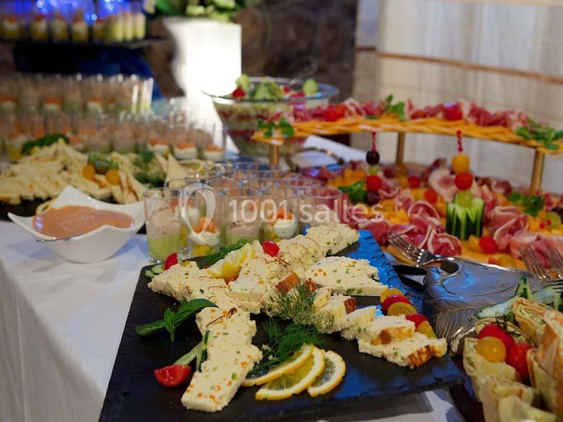 Plateau de fromages et charcuteries avec décorations de fruits et herbes, entouré d'autres plats sur une table de buffet.