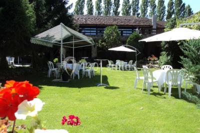 Grand jardin avec pelouse, arbres alignés et une structure couverte avec des tables et chaises blanches.