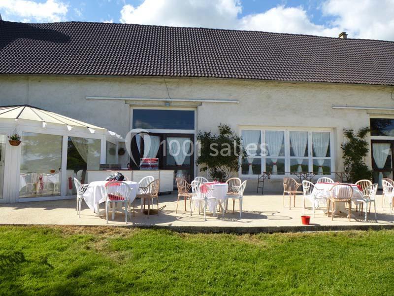 Terrasse d'un bâtiment avec des tables et chaises blanches disposées sur une pelouse, sous un ciel dégagé.