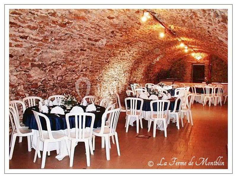 Salle voûtée en pierre aménagée avec des tables rondes dressées et des chaises blanches pour un événement.