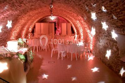 Salle voûtée en pierre avec éclairage rouge, tables basses, poufs et narguilés disposés dans une ambiance orientale.
