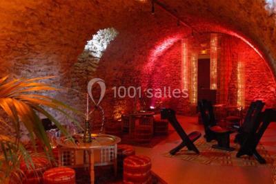 Salle voûtée en pierre avec éclairage rouge, tables basses, poufs et narguilés disposés dans une ambiance orientale.