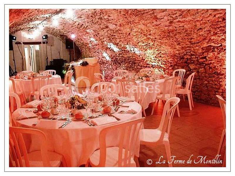Salle voûtée en pierre aménagée pour un repas, avec tables rondes dressées et chaises blanches.