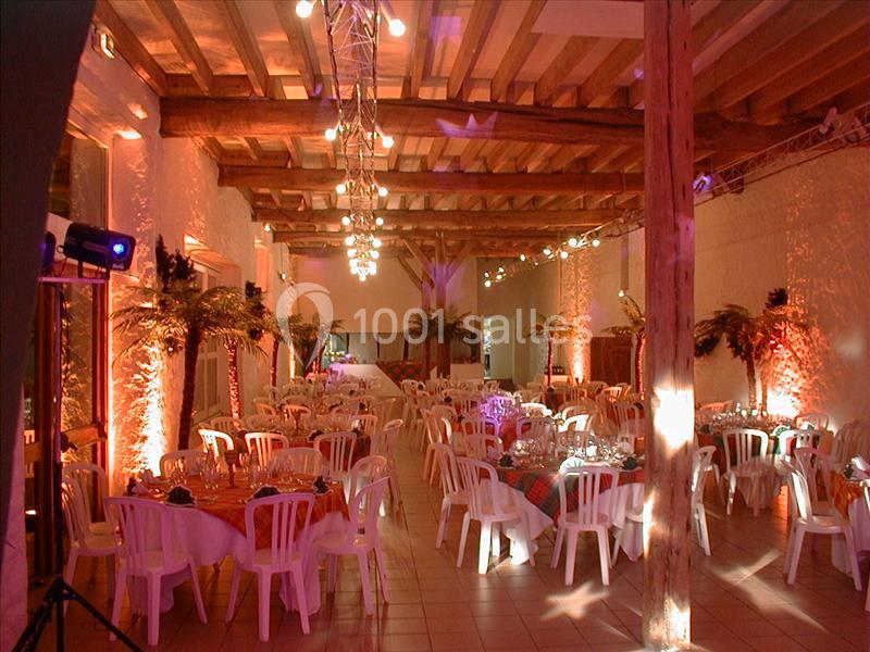 Salle de réception décorée avec des tables rondes, chaises blanches et éclairage chaleureux.