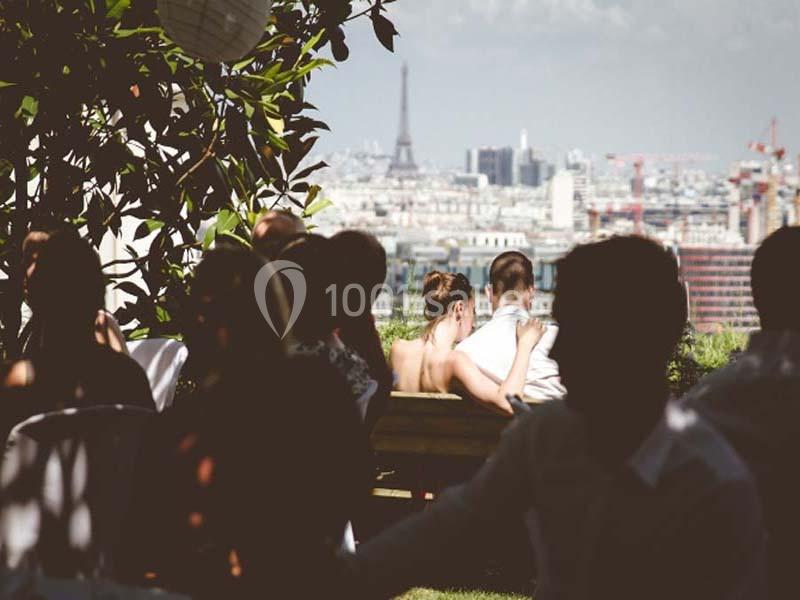 Un couple assis sur un banc profite d'une vue sur Paris avec la tour Eiffel en arrière-plan, entouré d'autres personnes.