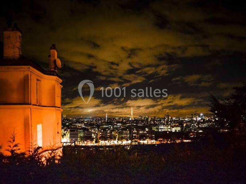 Vue nocturne d'une ville illuminée avec un bâtiment éclairé au premier plan et un ciel nuageux en arrière-plan.
