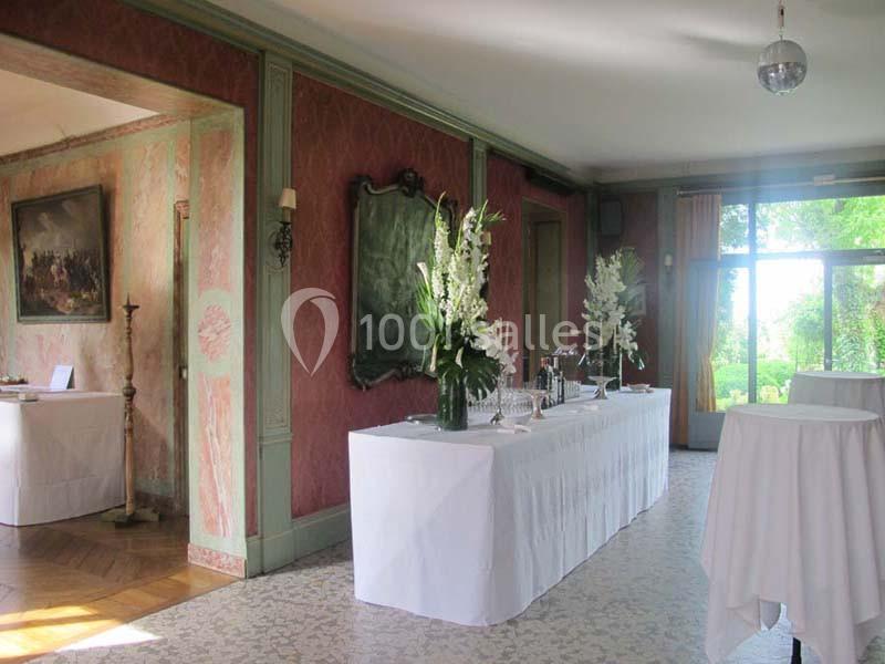 Salle lumineuse avec tables drapées de blanc, décorée de fleurs blanches et ouverte sur un jardin verdoyant.
