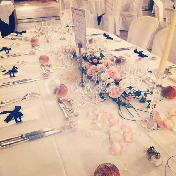 Table de réception élégamment dressée avec nappes blanches, fleurs roses, bougies et couverts disposés.