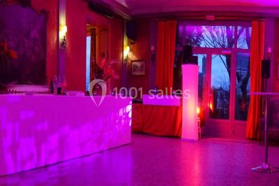 Salle de réception éclairée par des lumières violettes, avec un bar et des tables dans un décor chaleureux.