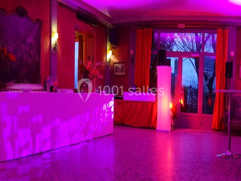 Salle de réception éclairée par des lumières violettes, avec un bar et des tables dans un décor chaleureux.
