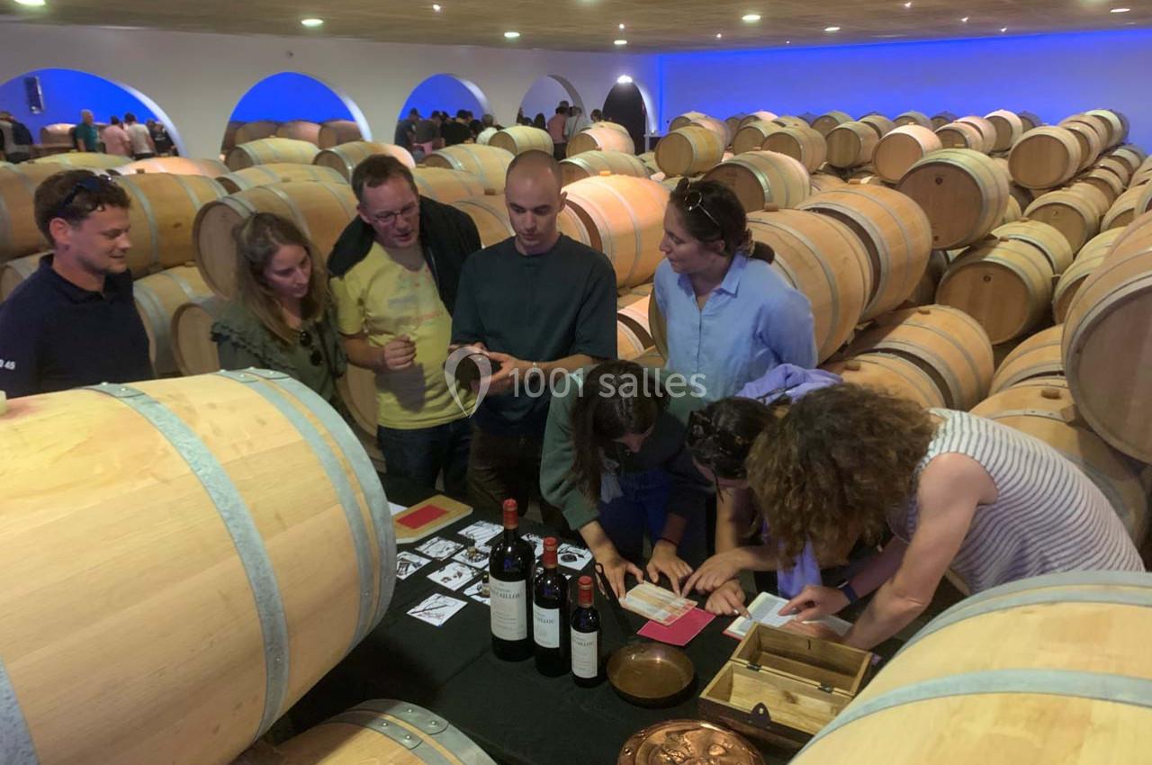 Des personnes participent à une activité autour du vin dans une cave avec des tonneaux en bois en arrière-plan.