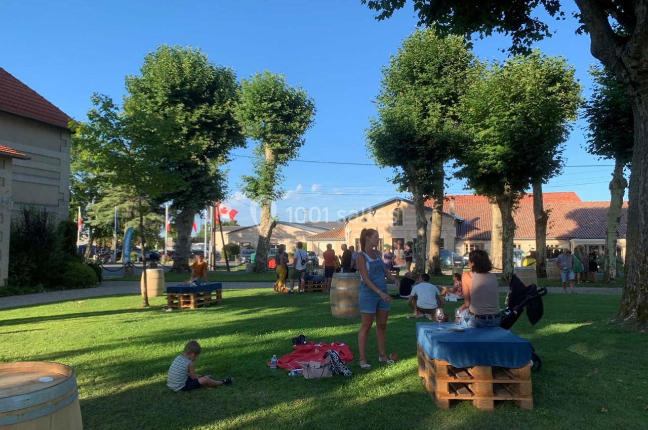 Des personnes se détendent dans un parc ombragé avec des tables en palettes, entourées d'arbres et de bâtiments.