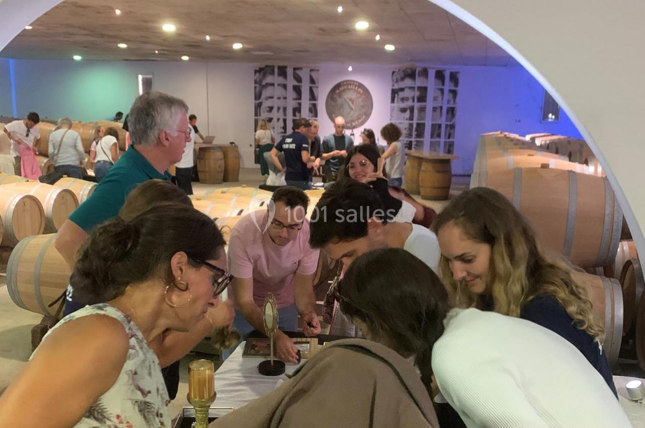 Des visiteurs observent une démonstration dans une cave à vin, entourés de tonneaux en bois et d'une ambiance lumineuse.