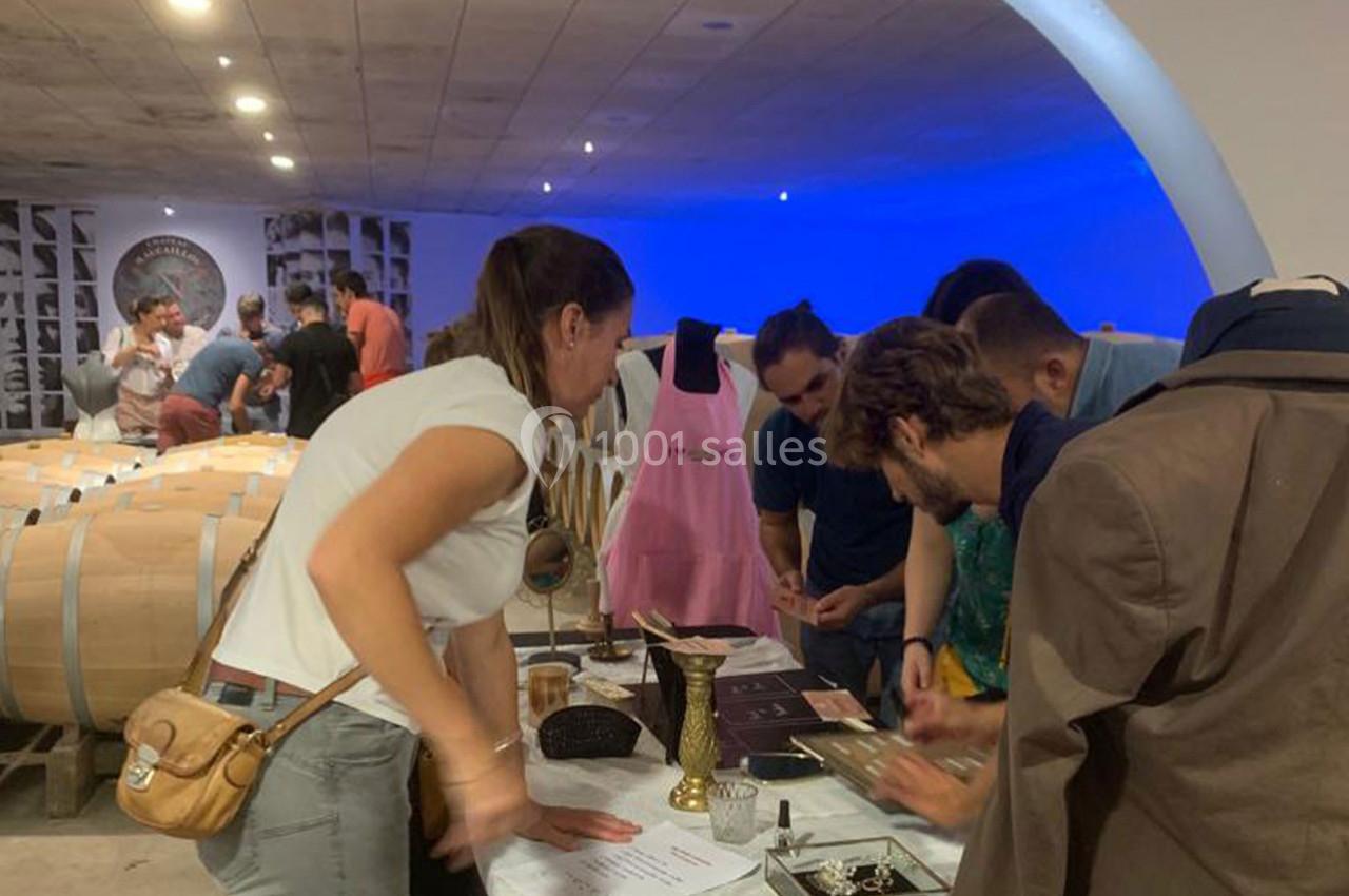 Des personnes participent à une activité interactive autour d'une table dans une cave à vin, entourées de tonneaux.