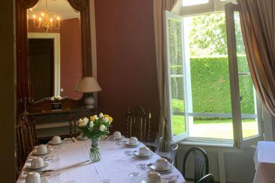 Salle à manger élégante avec table dressée, bouquet de fleurs au centre, grande fenêtre ouverte sur un jardin verdoyant.
